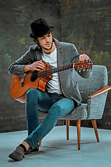 Image showing Cool guy with hat playing guitar on gray background