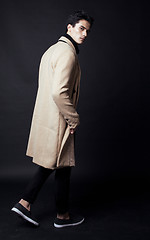 Image showing cool real young man in coat on black background posing