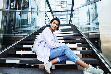 Image showing young cute modern indian girl at university building sitting on stairs reading a book, wearing hipster glasses, lifestyle people concept