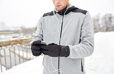 Image showing man in earphones with smartphone on winter bridge