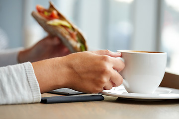 Image showing woman drinking coffee and eating sandwich at cafe