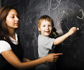 Image showing little cute boy with young teacher in classroom studying at blackboard smiling, lifestyle people concept