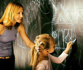 Image showing portrait of mature woman teacher with little cute blonde girl pupil writing on blackboard together, lifestyle people concept