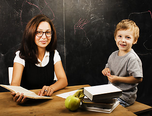 Image showing little cute boy with young teacher in classroom studying at blackboard smiling, lifestyle people concept