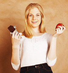 Image showing young beauty blond teenage girl eating chocolate smiling, choice