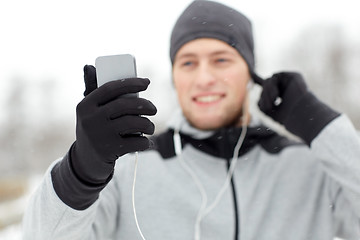 Image showing happy man with earphones and smartphone in winter