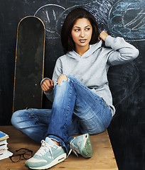 Image showing young cute teenage girl in classroom at blackboard seating on ta