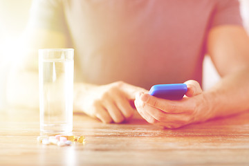 Image showing close up of hands with smartphone, pills and water