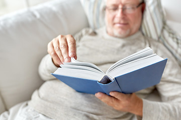 Image showing senior man lying on sofa and reading book at home