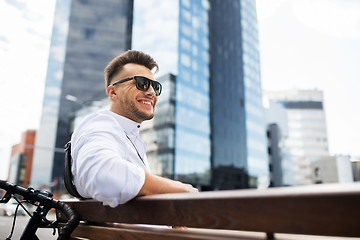 Image showing happy young man with bicycle sitting on city bench