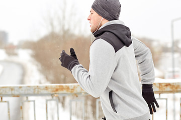 Image showing man in earphones running along winter bridge