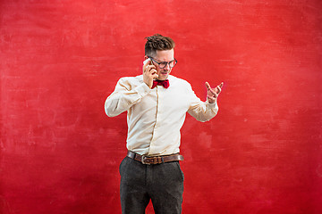 Image showing Portrait of puzzled man talking by phone a red background