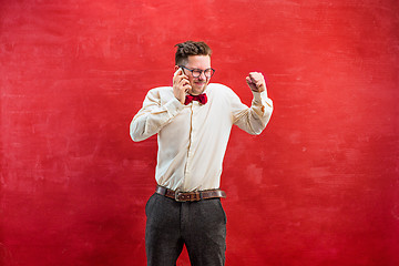 Image showing Portrait of puzzled man talking by phone a red background