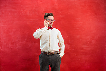 Image showing Portrait of puzzled man talking by phone a red background