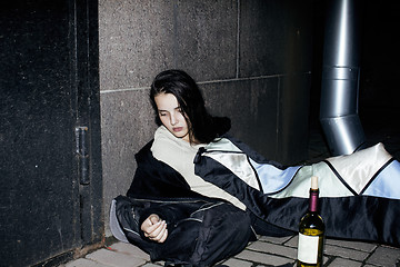 Image showing young poor ttenage girl sitting at dirty wall on floor with bottle of vine, poor refugee alcoholic, hopeless homeless woman in depression, real junky concept