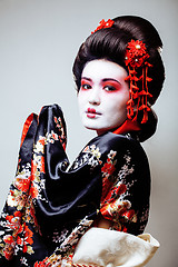 Image showing young pretty geisha in black kimono among sakura, asian ethno