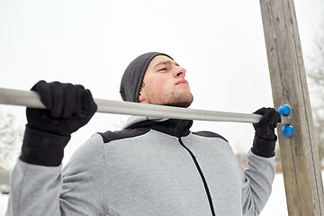 Image showing young man exercising on horizontal bar in winter