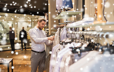 Image showing happy young man choosing clothes in clothing store