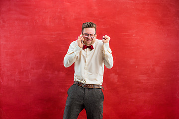 Image showing Portrait of puzzled man talking by phone a red background