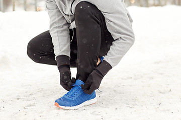 Image showing man with earphones tying sports shoes in winter