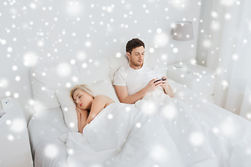 Image showing man texting message while woman is sleeping in bed