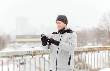 Image showing happy man with earphones and smartphone in winter