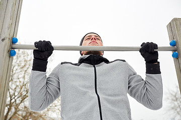 Image showing young man exercising on horizontal bar in winter