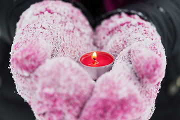 Image showing close up of hands in winter mittens holding candle