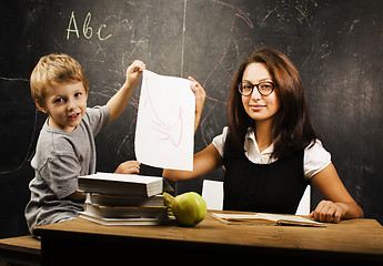 Image showing little cute boy with young teacher in classroom studying at blac