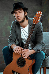 Image showing Cool guy sitting with guitar on gray background