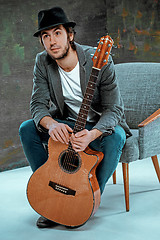 Image showing Cool guy sitting with guitar on gray background