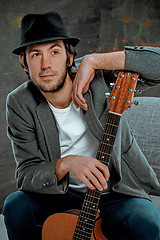 Image showing Cool guy sitting with guitar on gray background