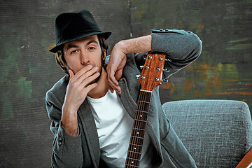 Image showing Cool guy sitting with guitar on gray background