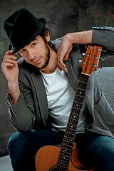 Image showing Cool guy sitting with guitar on gray background