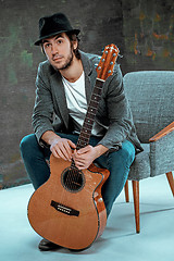 Image showing Cool guy sitting with guitar on gray background