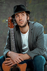 Image showing Cool guy sitting with guitar on gray background