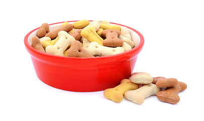 Image showing Dry dog food in a red bowl, biscuits spilled beside