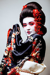 Image showing young pretty geisha in black kimono among sakura, asian ethno