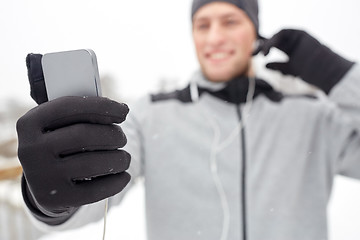 Image showing happy man with earphones and smartphone in winter