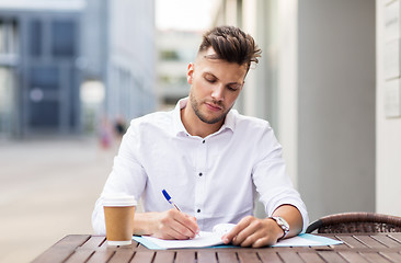 Image showing man with coffee and folder writing at city cafe