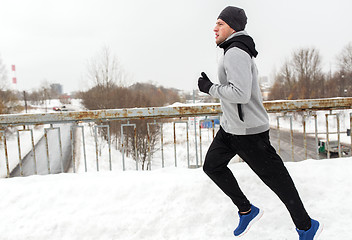 Image showing man in earphones running along winter bridge