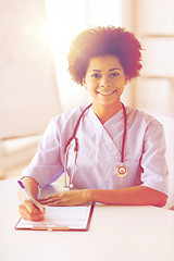 Image showing happy female doctor or nurse writing to clipboard