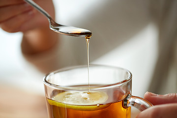 Image showing close up of woman adding honey to tea with lemon