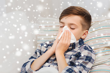 Image showing ill boy lying in bed and blowing his nose at home