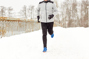 Image showing man in earphones running along winter bridge