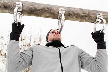 Image showing young man exercising on horizontal bar in winter