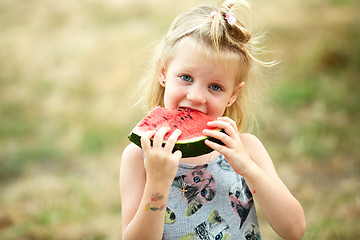 Image showing Adorable blonde girl eats a slice of watermelon outdoors