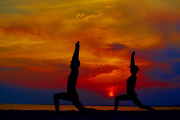 Image showing Yoga people training and meditating in warrior pose outside by beach at sunrise or sunset.