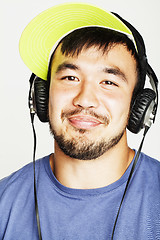 Image showing young asian man in hat and headphones listening music on white b