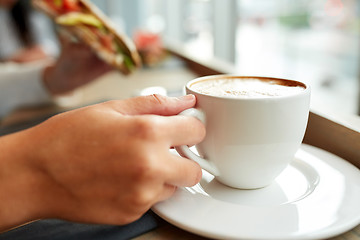 Image showing woman drinking coffee and eating sandwich at cafe